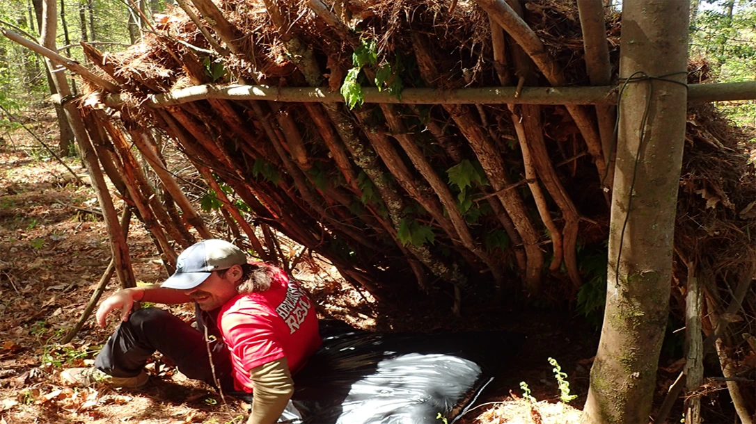 In a survival class, a student tries out the plastic garbage mattress under a lean-to.